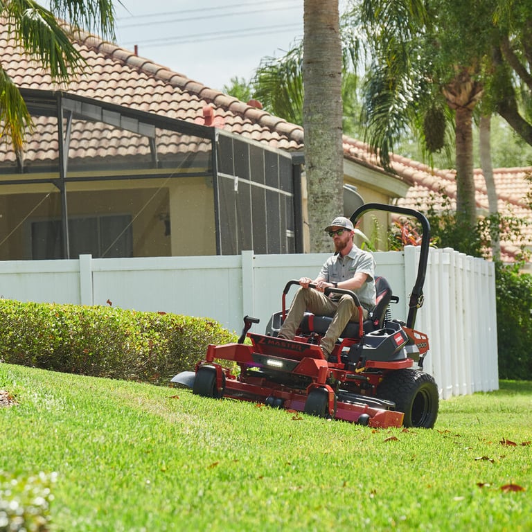 Man mowing a backyard lawn on a red Toro Z Master 2000 zero-turn mower beside a white fence